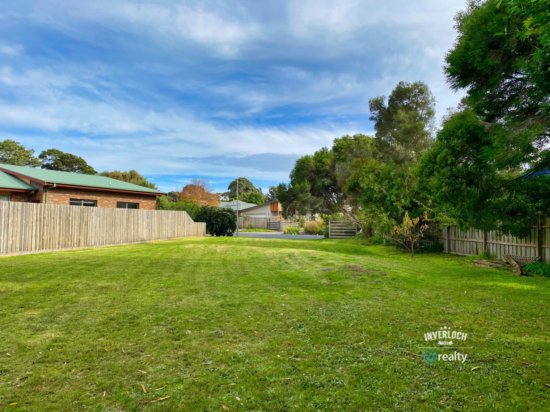 A large lawn with a wooden fence and a house in the background.