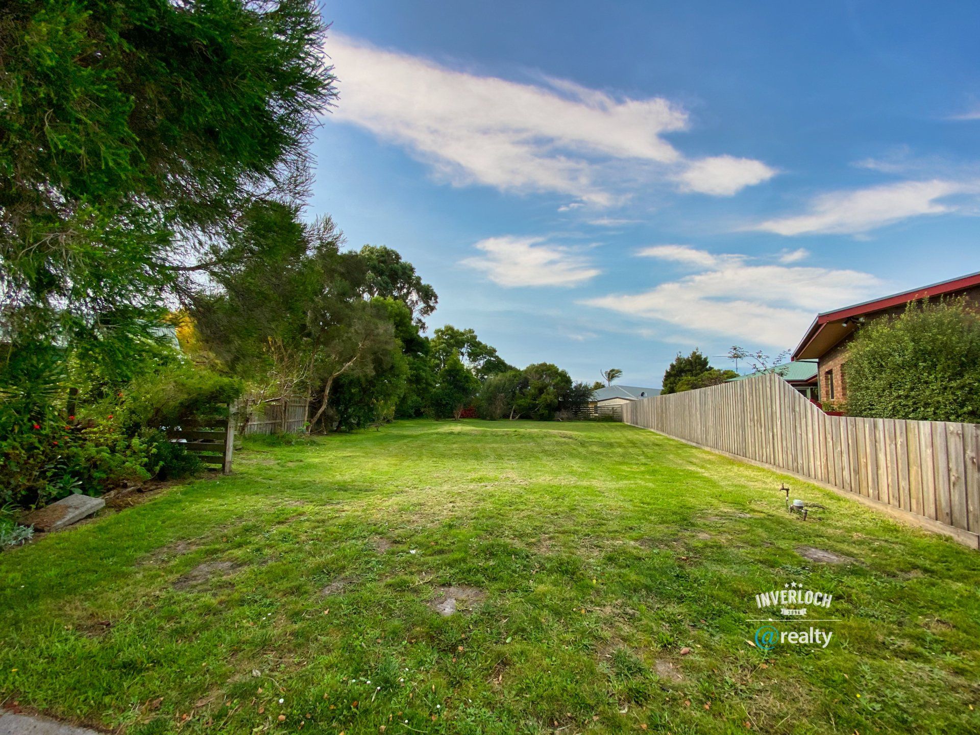 A lush green field with a wooden fence and trees in the background.