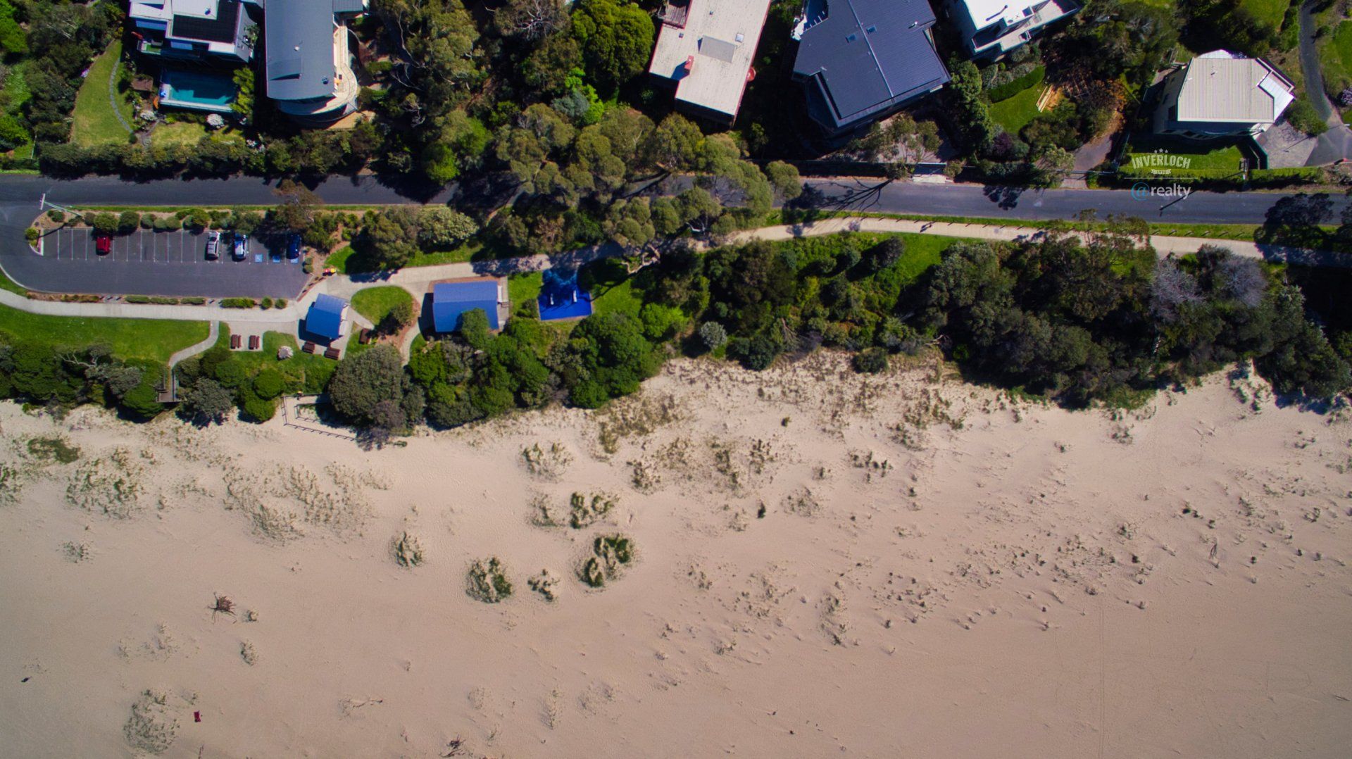 An aerial view of a beach with houses and trees in the background.