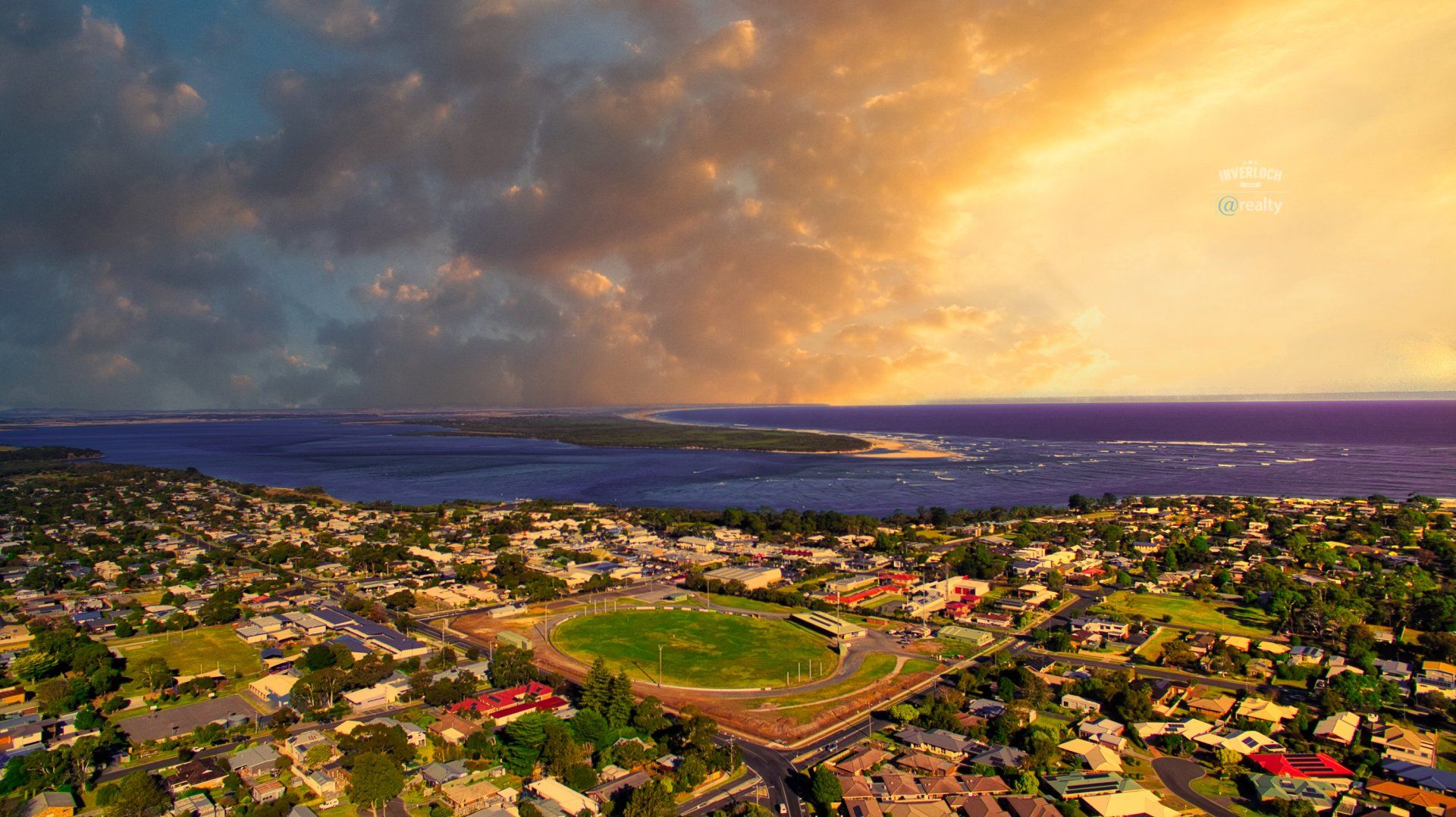 An aerial view of a city with a baseball field and a sunset in the background.