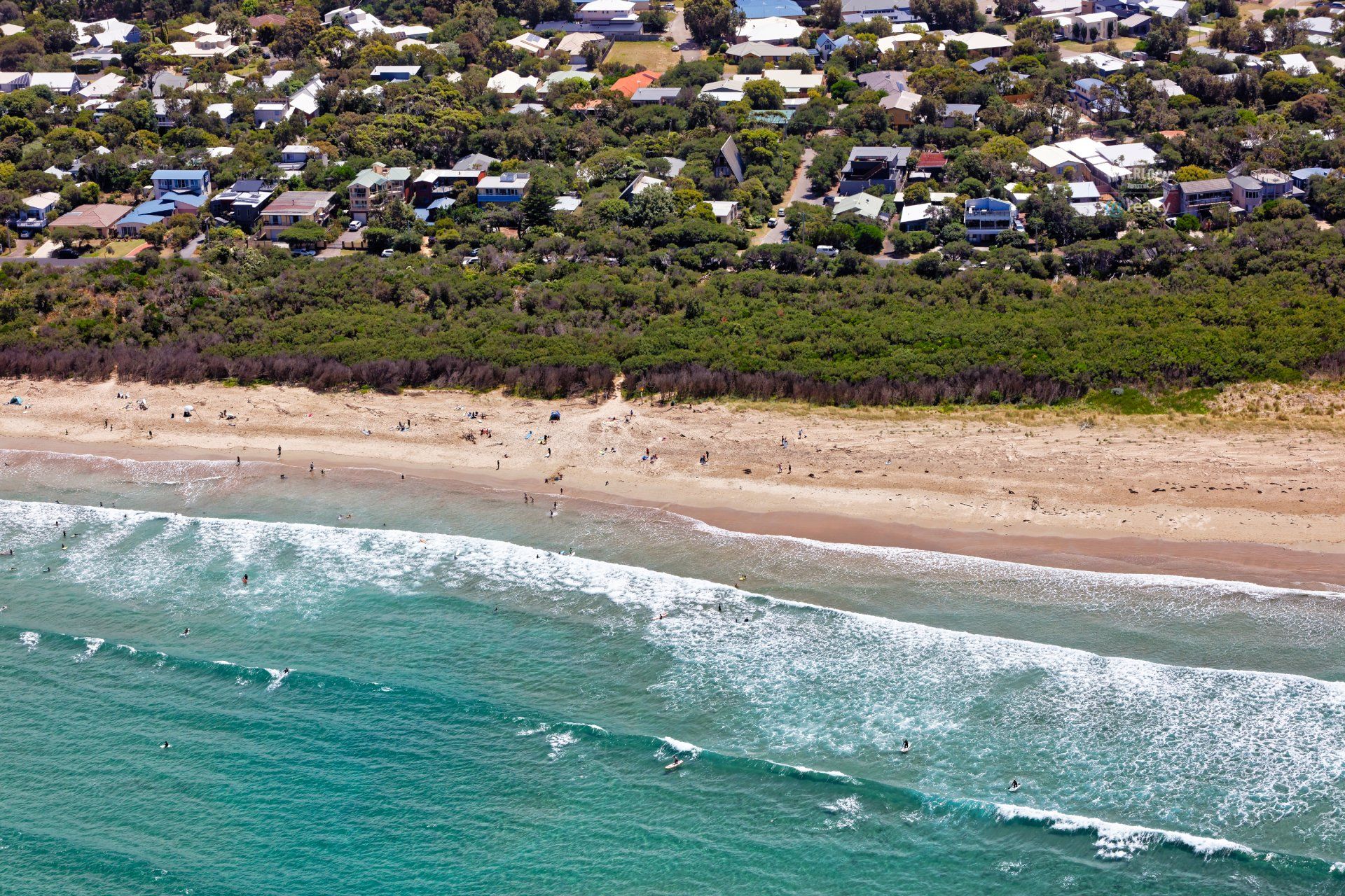 An aerial view of a beach with waves and houses in the background.