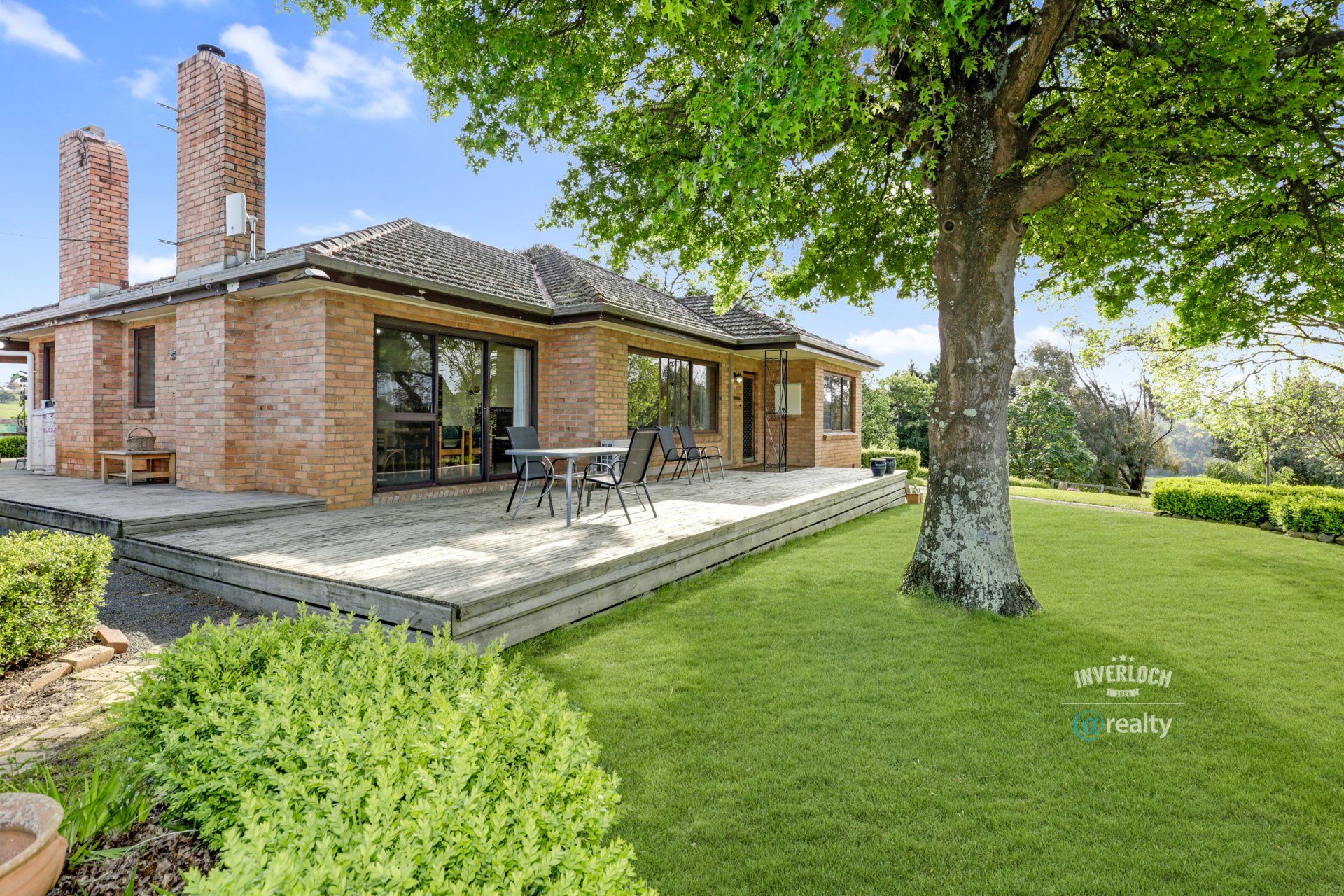 A large brick house with a large deck and a tree in front of it.