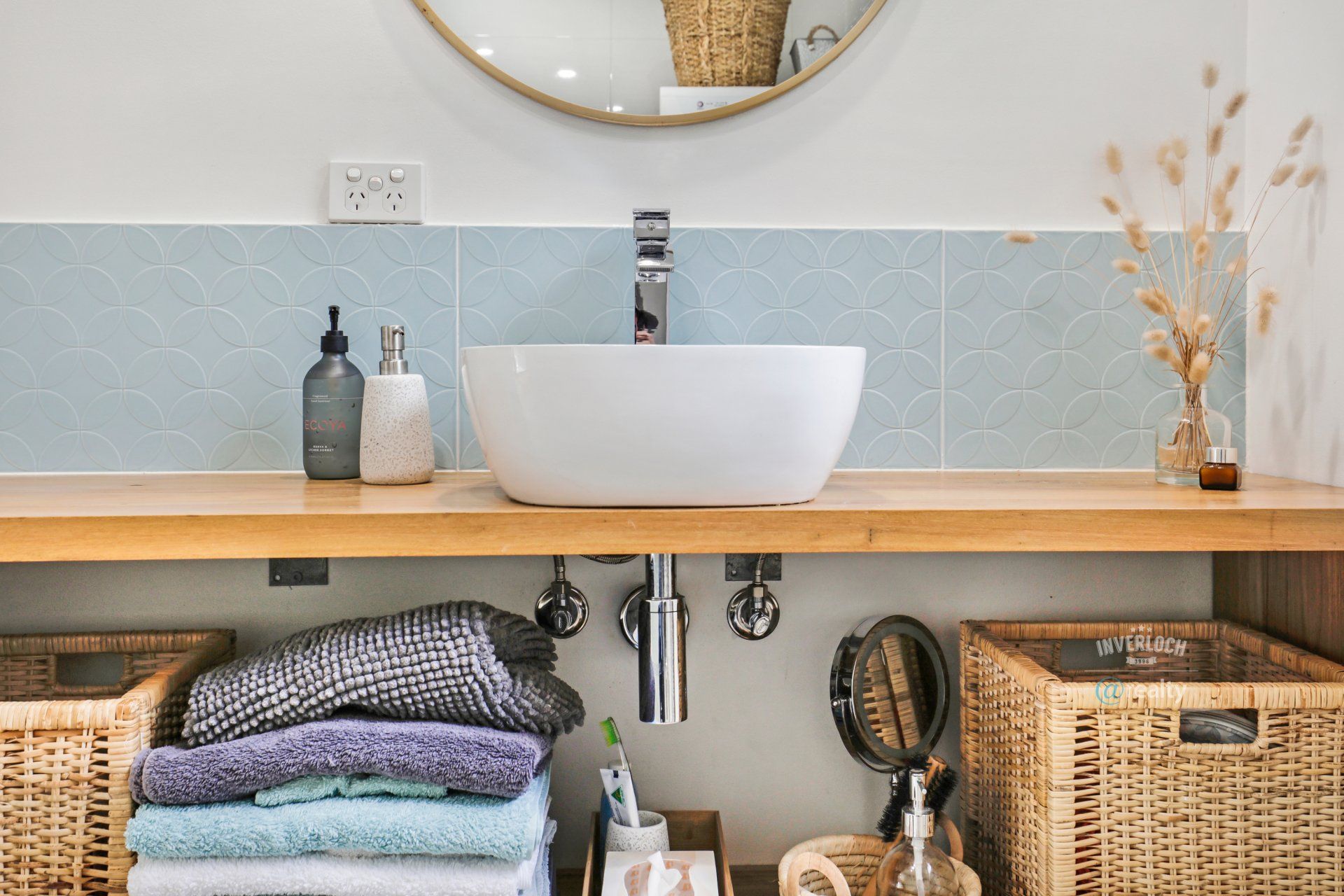 A bathroom with a sink , mirror , baskets and towels.