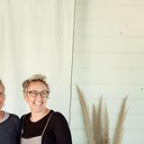 A man and a woman are posing for a picture in front of a white wall.