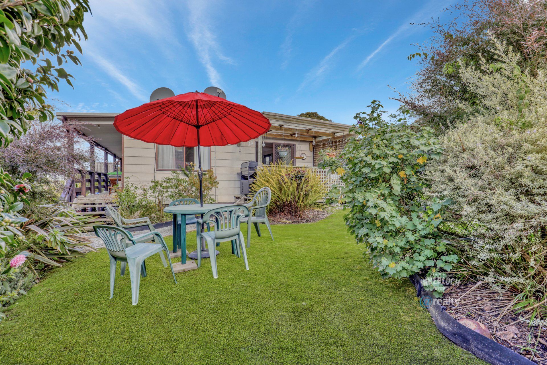 A lawn with a table and chairs and an umbrella in front of a house.