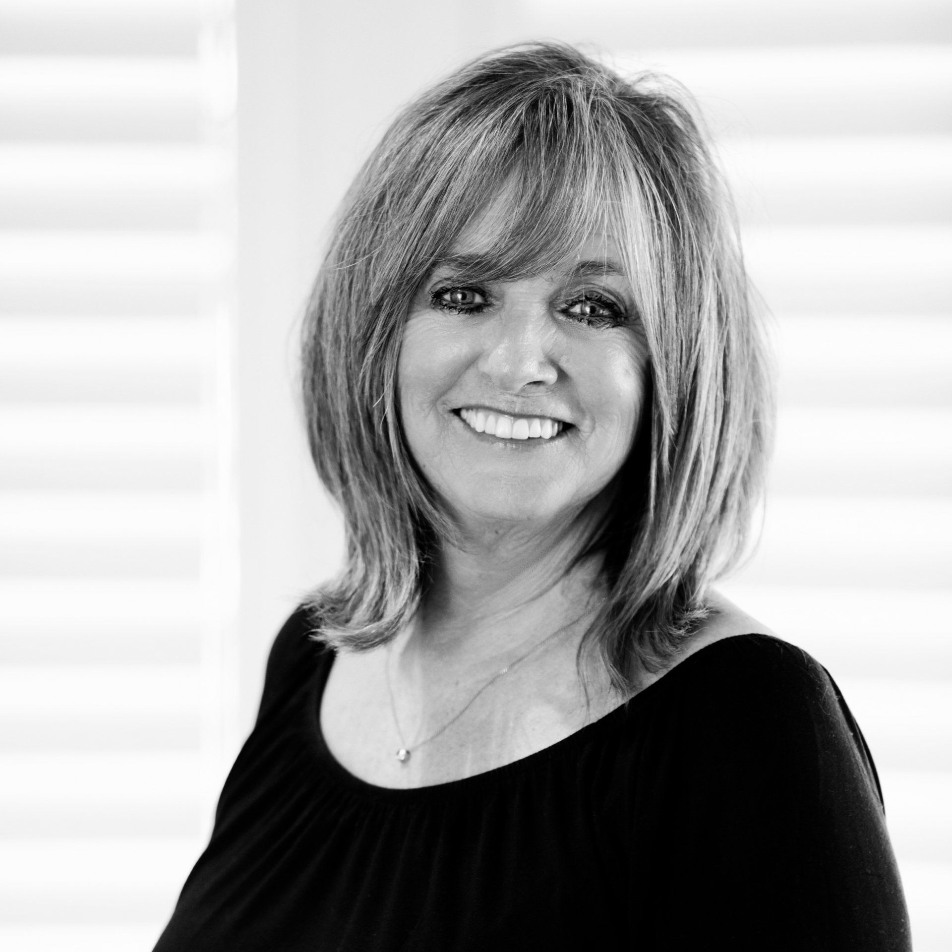 A woman in a black shirt is smiling in a black and white photo.
