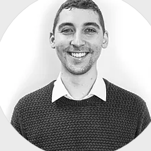 A black and white photo of a man wearing a sweater and smiling.