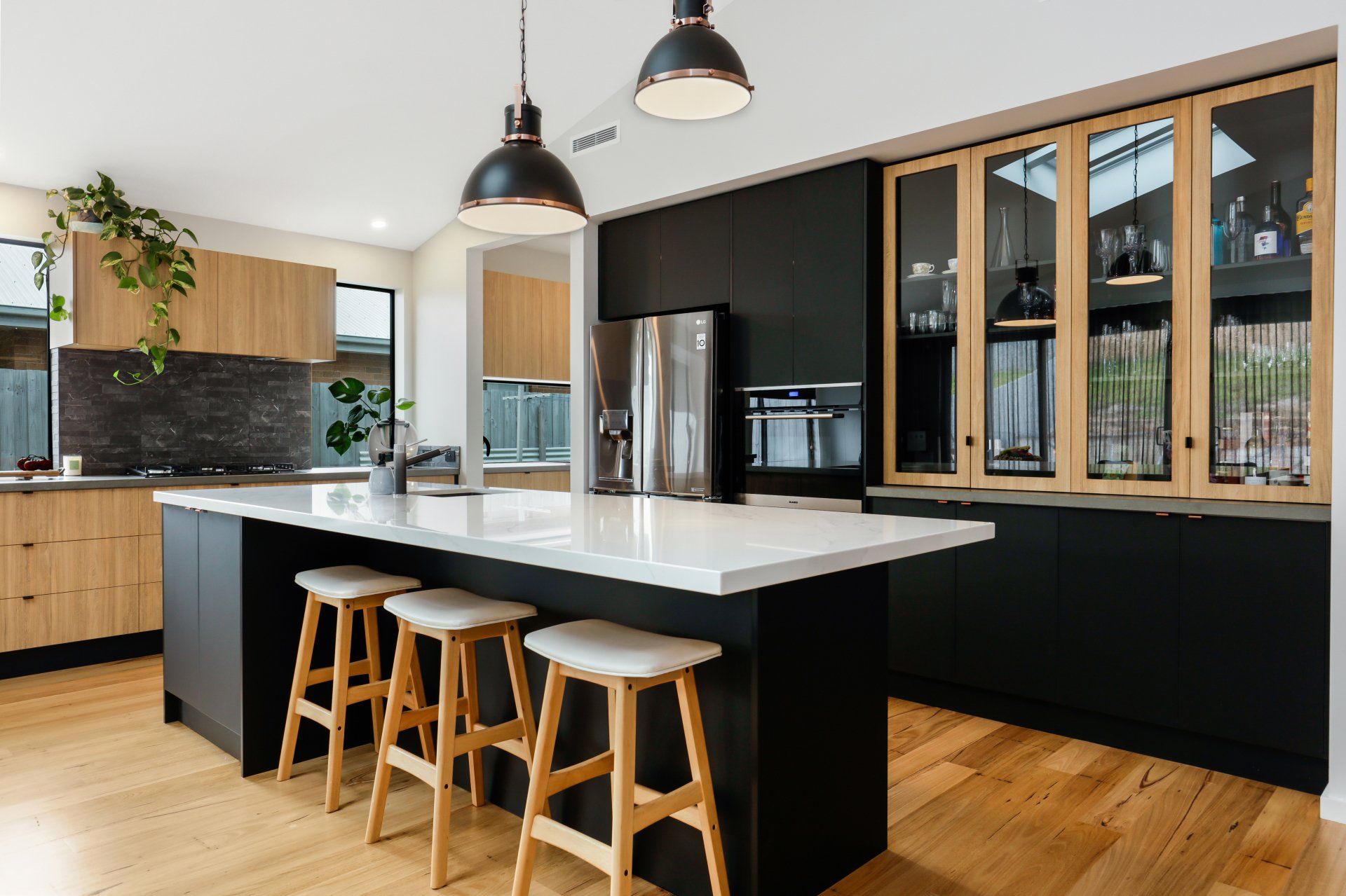 A kitchen with black cabinets and wooden floors and a large island with stools.