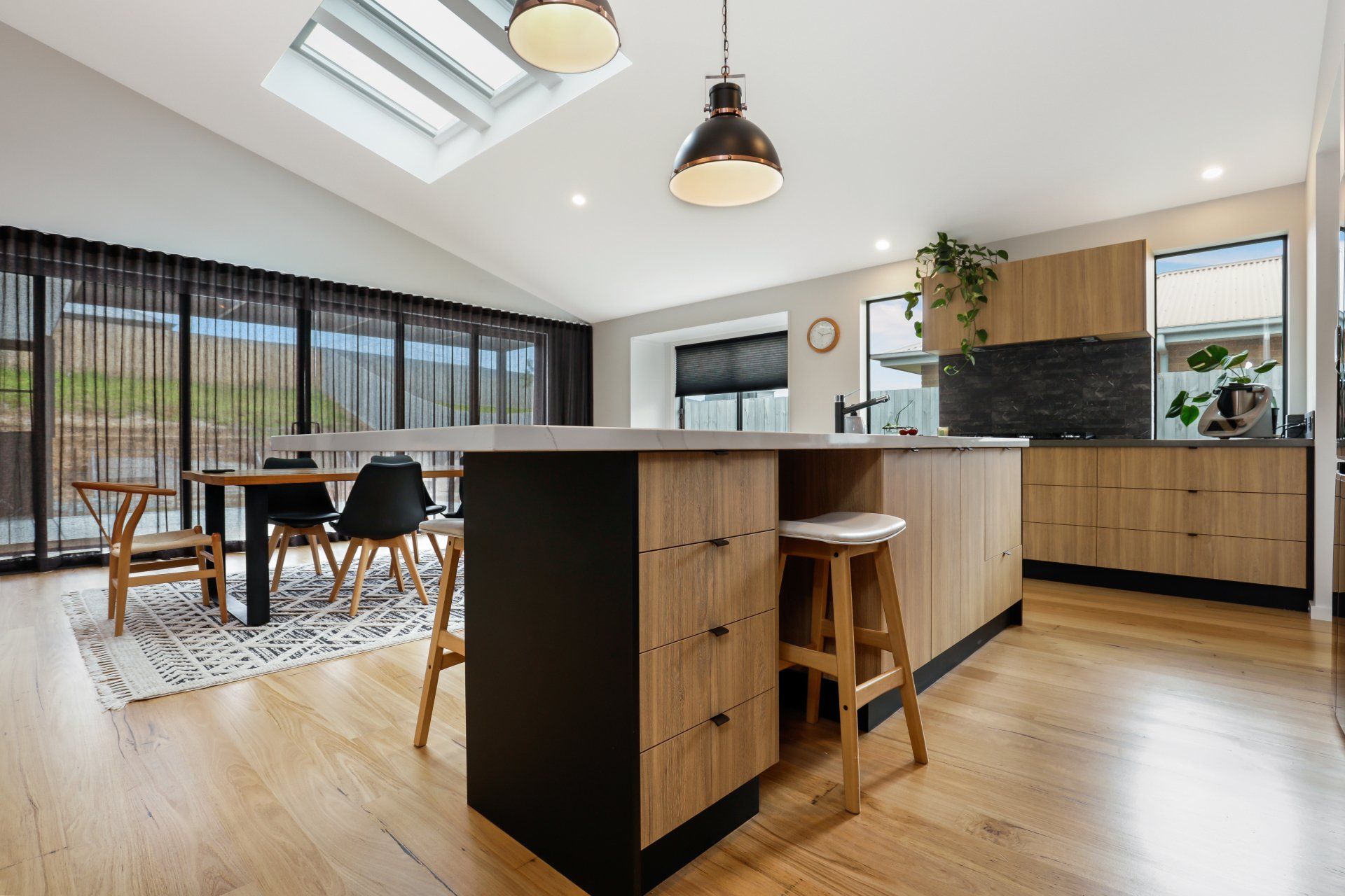 A kitchen with wooden cabinets , stools , a table and a skylight.