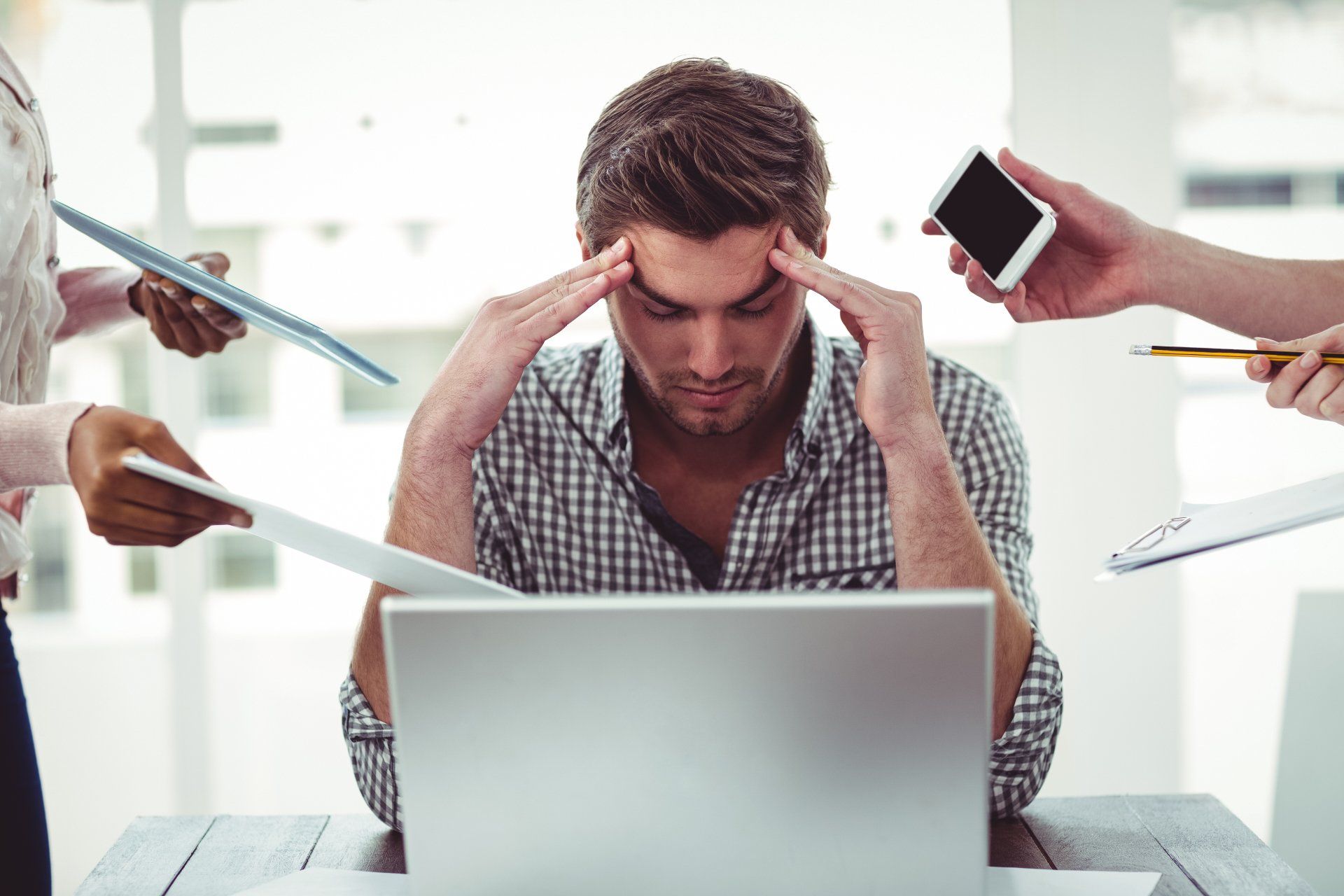 A man is sitting in front of a laptop computer with his hands on his head.
