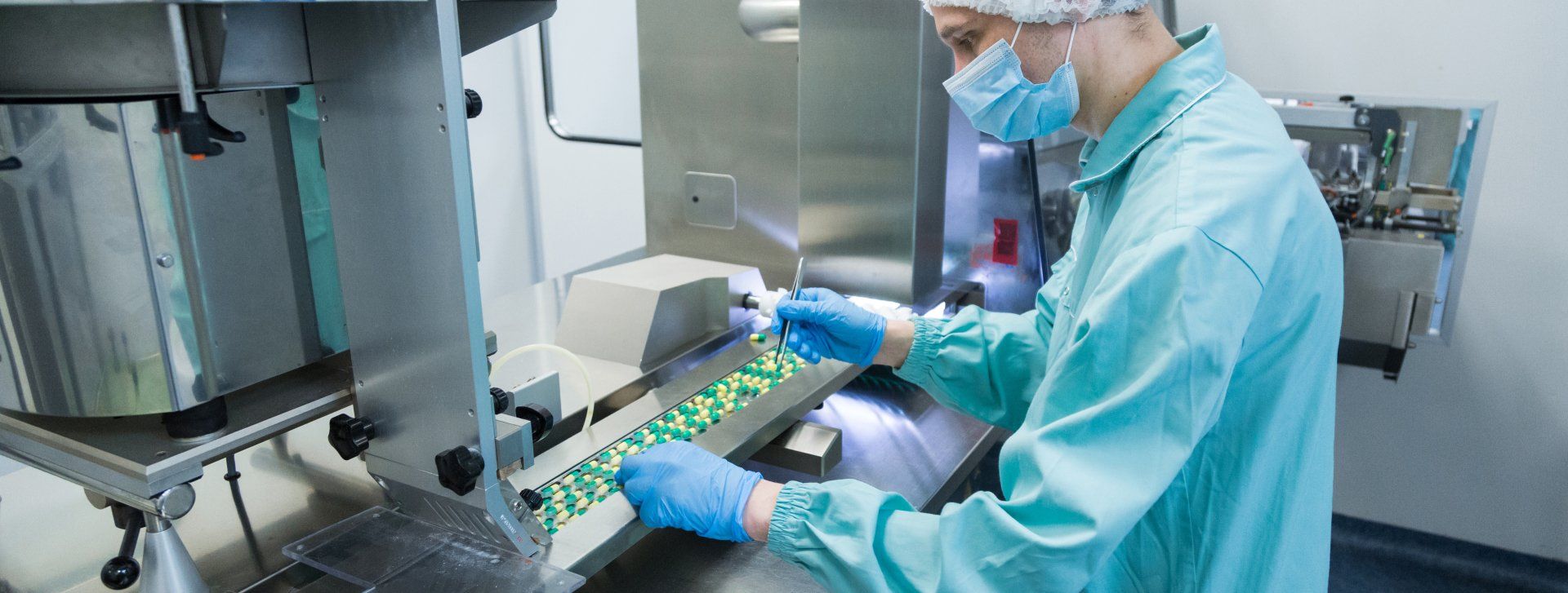 A man wearing a mask and gloves is working on a machine in a clean room.