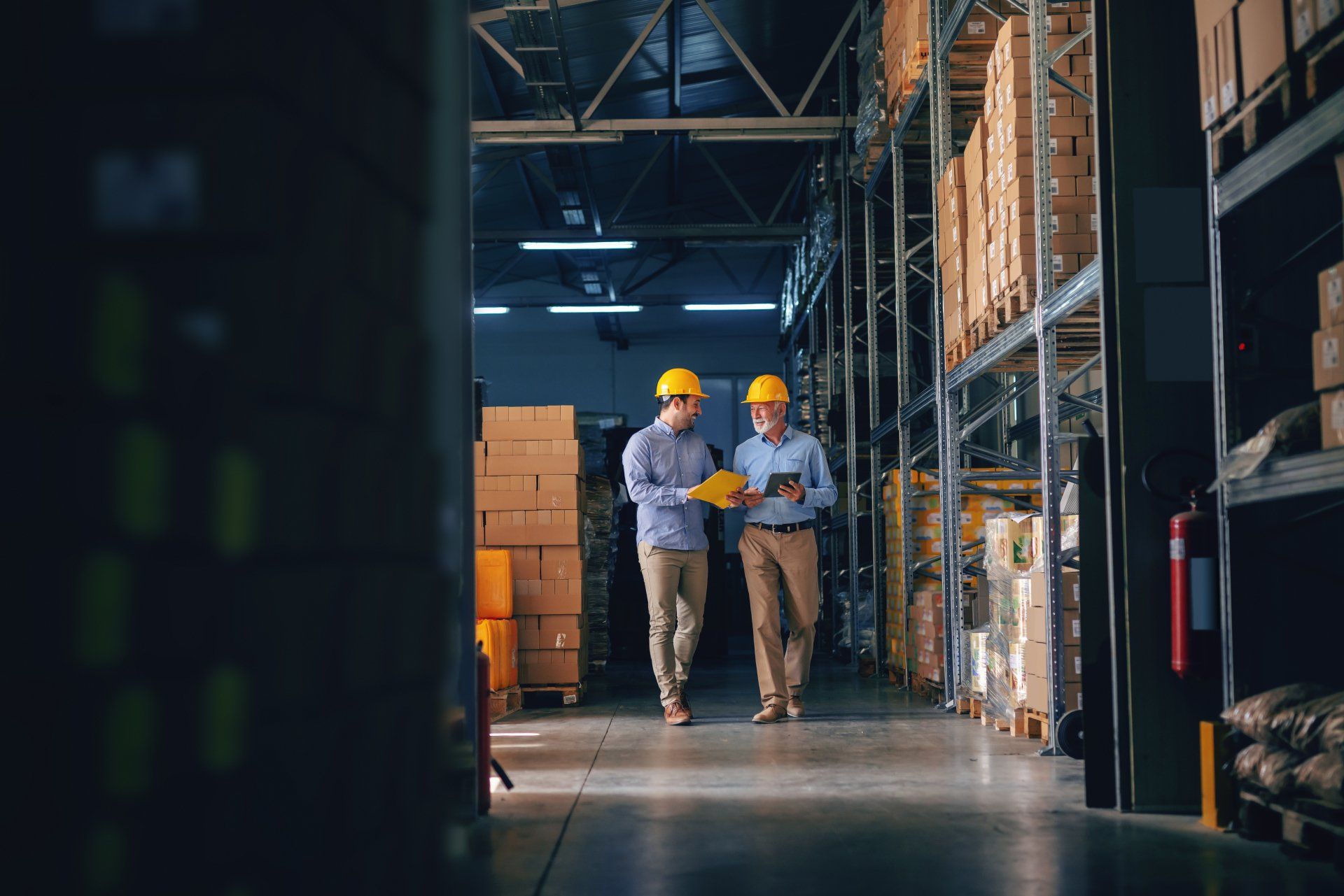 Two men are walking through a warehouse looking at a tablet.