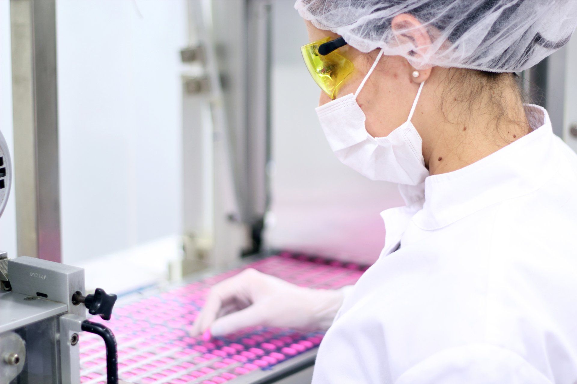 A woman in a lab coat and mask is working on a machine.