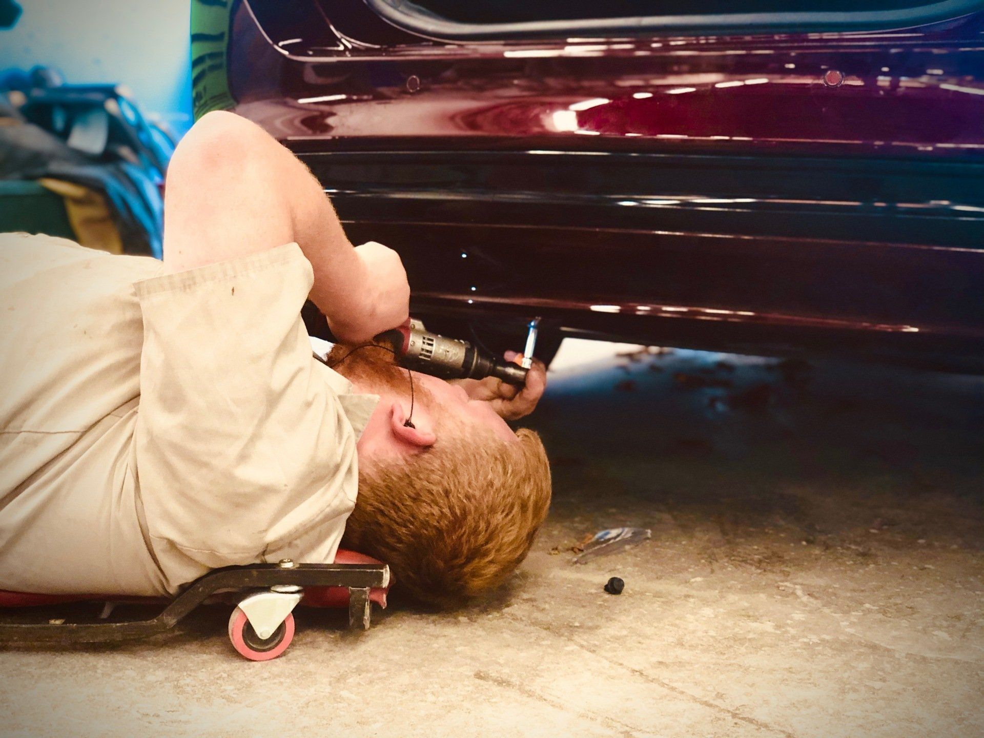 Mechanic lying under a red car, using a tool near the undercarriage in a garage