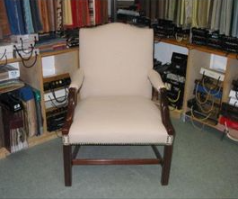 Cream-colored upholstered armchair with dark wooden frame. In a fabric store, surrounded by fabric swatches.