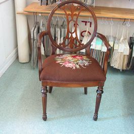 Wooden chair with circular back and floral embroidery on a brown seat.