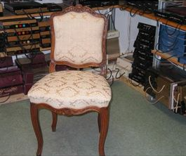 Upholstered antique chair with curved legs in front of audio equipment.