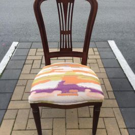 Wooden chair with colorful patterned seat cushion on a brick and asphalt surface.