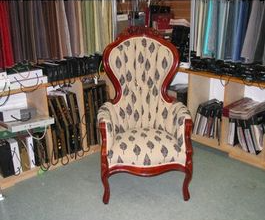 Ornate wooden armchair with leaf-patterned fabric in a fabric store, surrounded by fabric swatches.