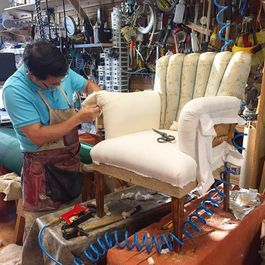 Man upholstering a chair in a workshop, stapling fabric. Workshop background with tools.