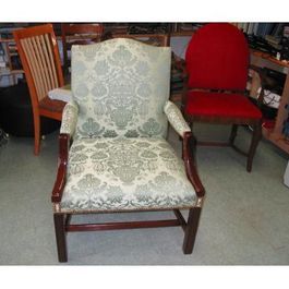 Upholstered armchair with light blue damask pattern, surrounded by other chairs in a cluttered room.