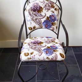 Metal chair with floral patterned seat and back, set against a wall.