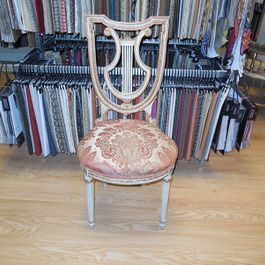 Antique chair with shield-shaped back and patterned cushion in front of fabric samples.
