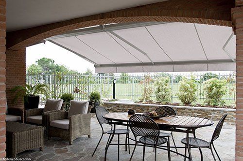 una veranda con un tavolo, delle poltrone da esterno e un tendone