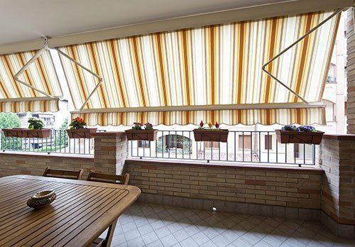una terrazza con un tavolo e due tendoni a righe di color beige e arancione