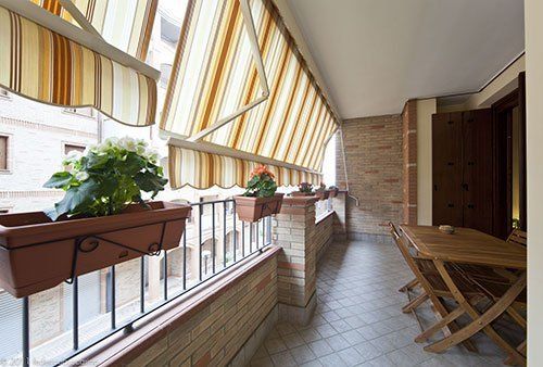 un balcone lungo con dei tendoni di color arancione e beige a righe