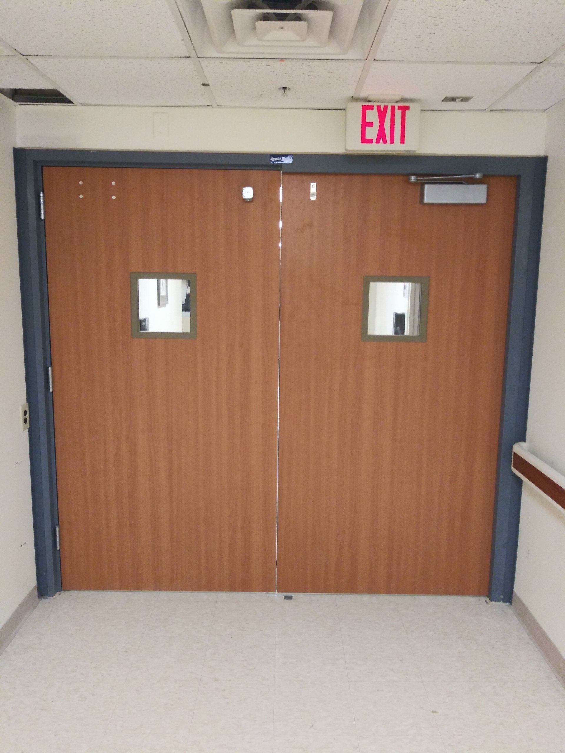 Wooden double exit doors in a hallway with red EXIT sign above them