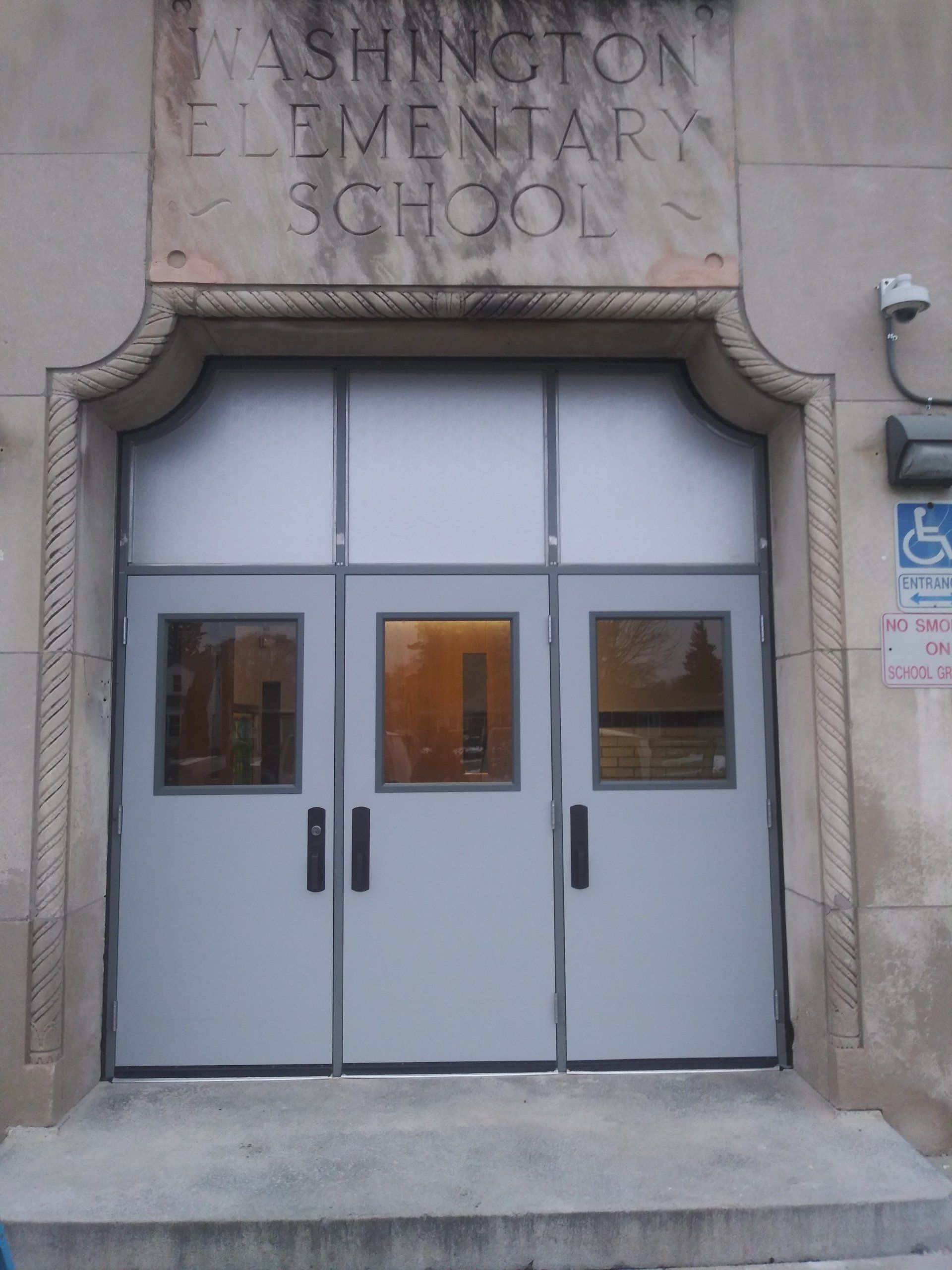 Closed double doors at Washington Elementary School entrance with stone arch and accessibility sign nearby