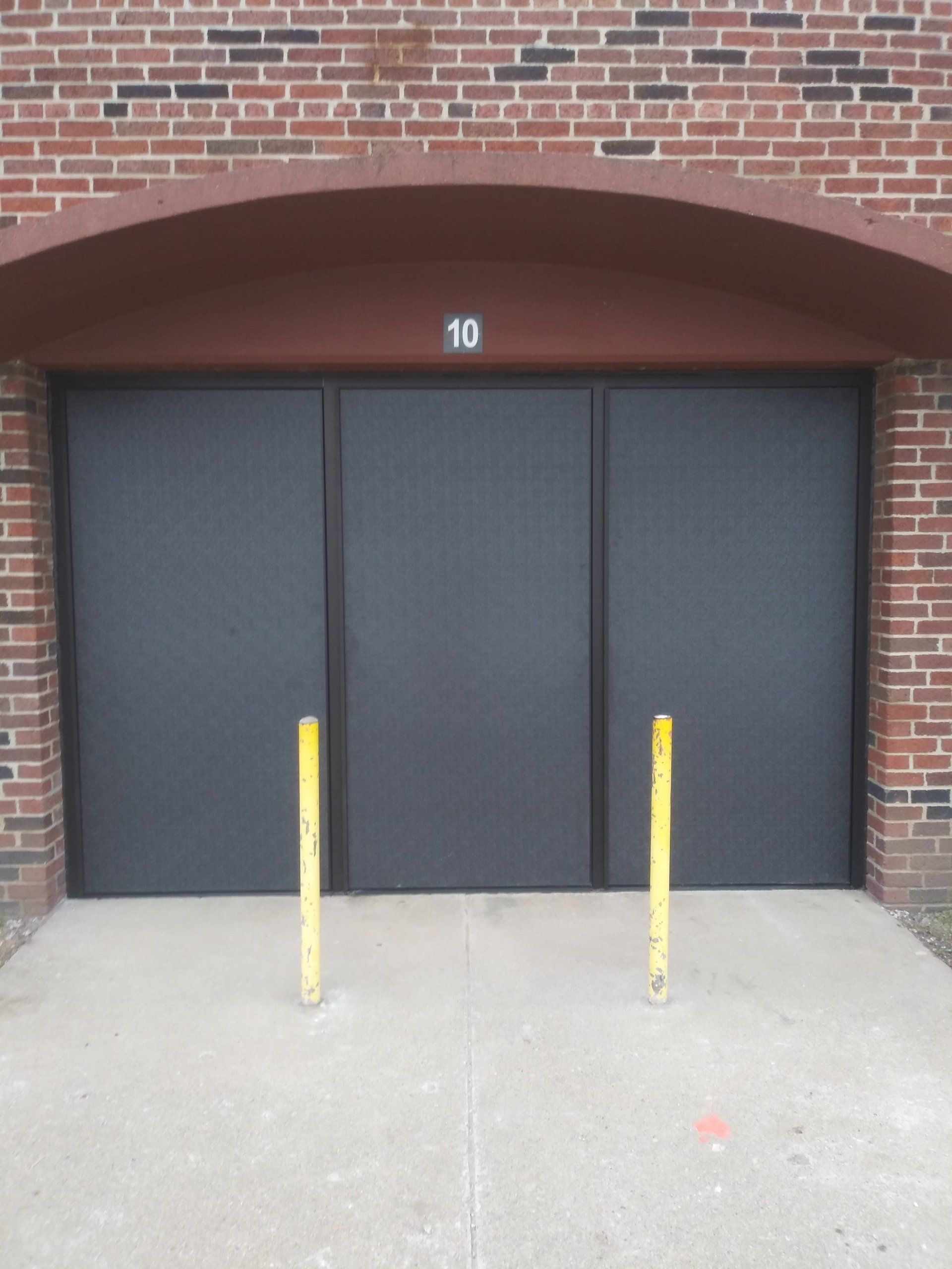 Brick building entrance with dark doors and two yellow bollards in front