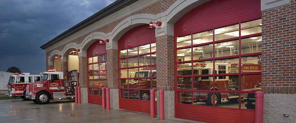 Fire station exterior with red garage doors and fire trucks.