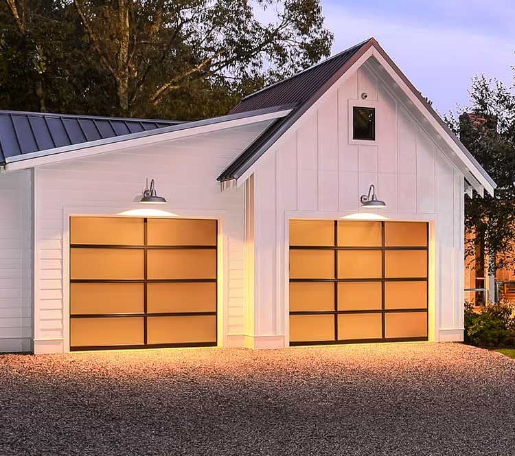 White garage with two lit orange doors and exterior lamps at dusk