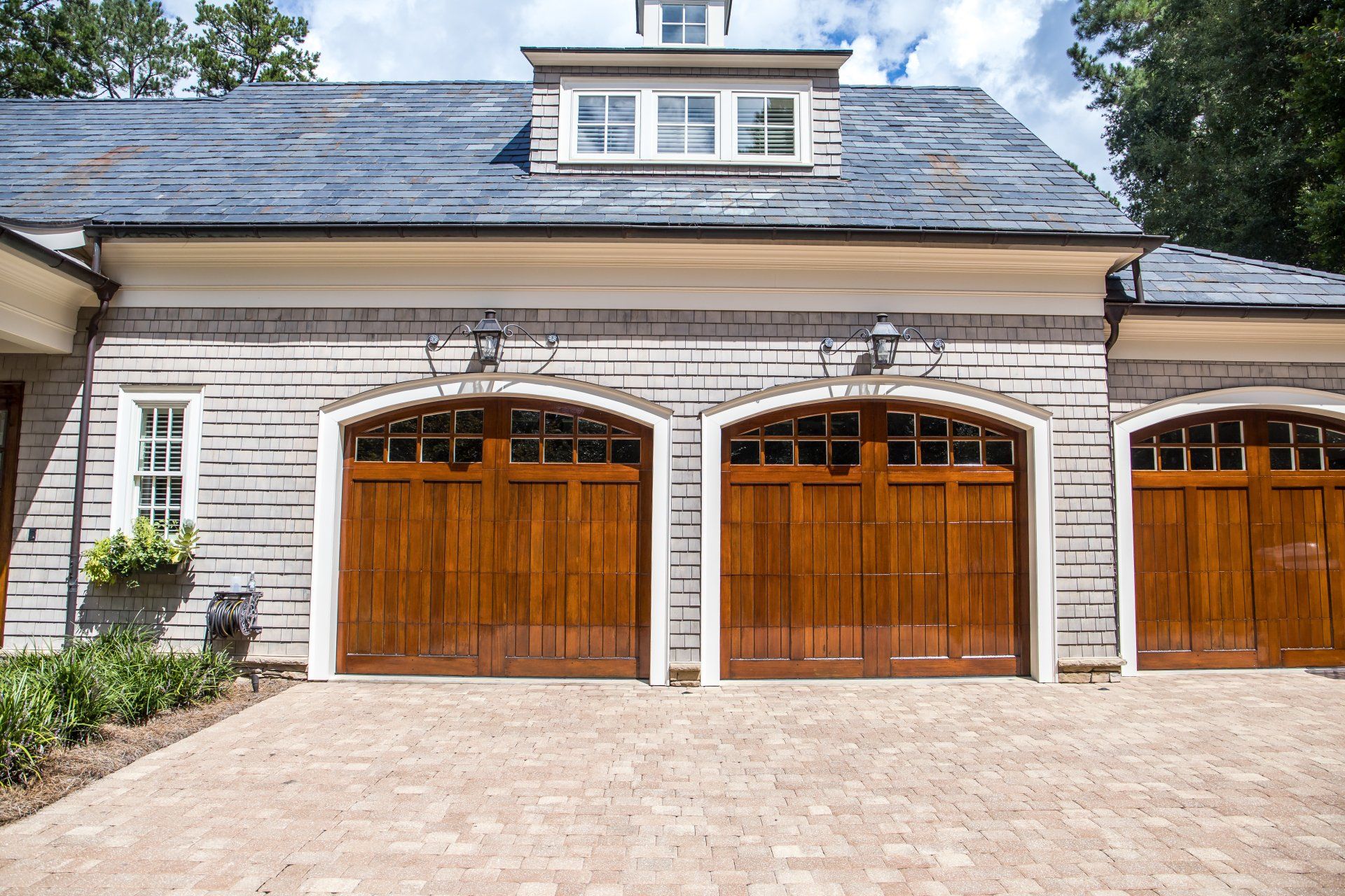 Three-bay garage with wooden doors and a stone driveway. The building is gray and has a blue roof.