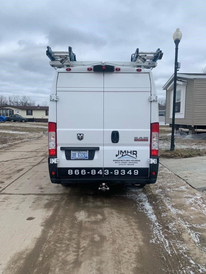 White work van parked on a driveway with a ladder rack. The van has business information and a license plate.