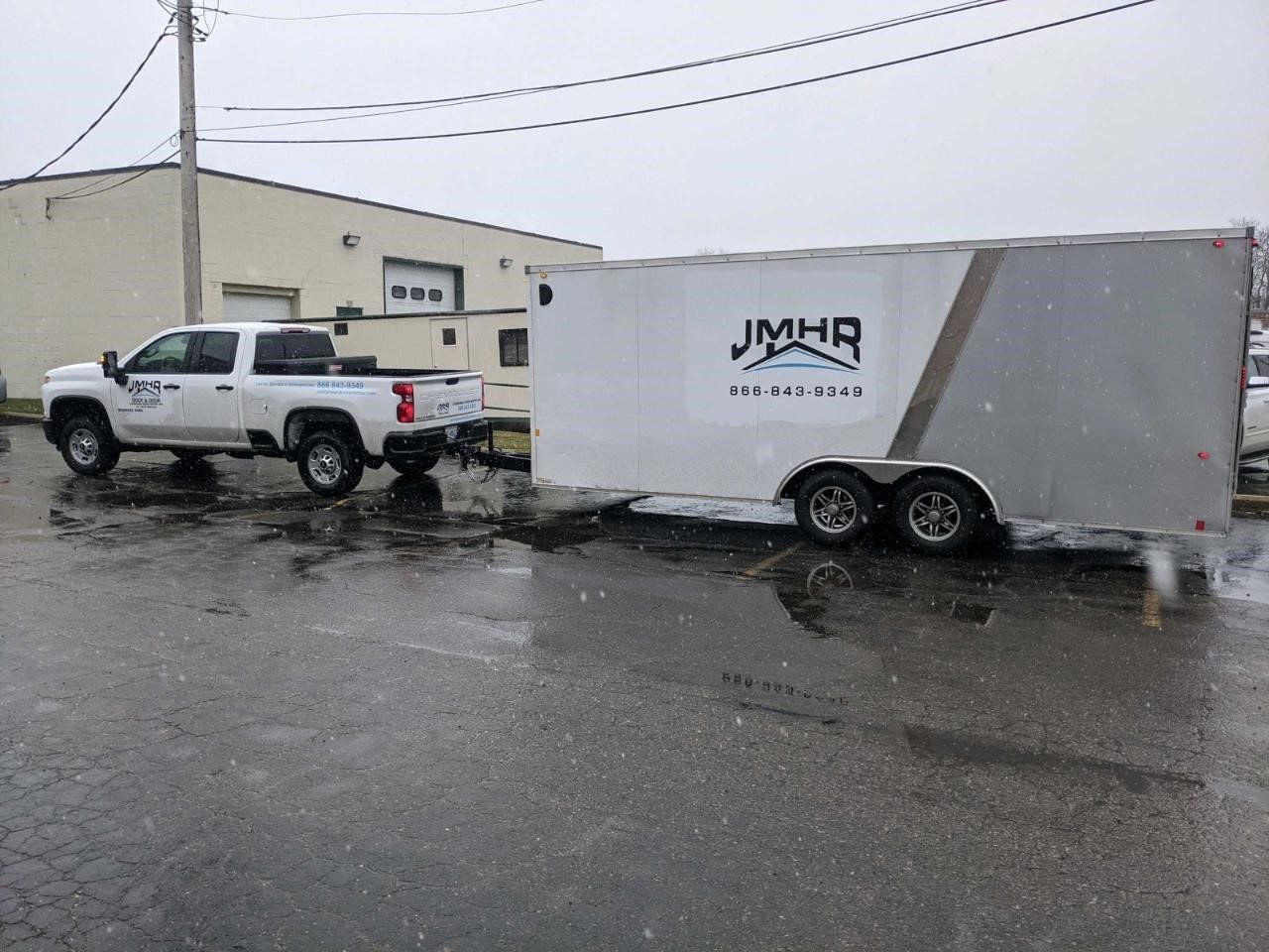 White truck towing an enclosed trailer with company logo in a wet, snowy parking lot.