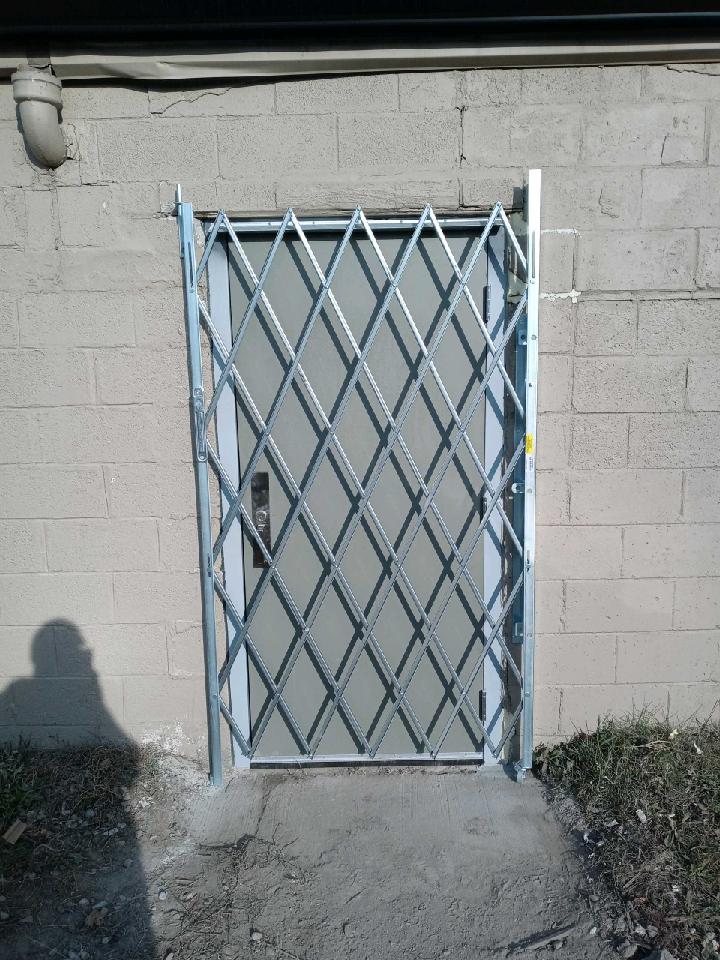 Blue metal security gate across a cinderblock doorway in a small concrete yard.
