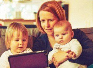 Mother sat on sofa with 2 children looking at a tablet. Return to work and career break online seminars.