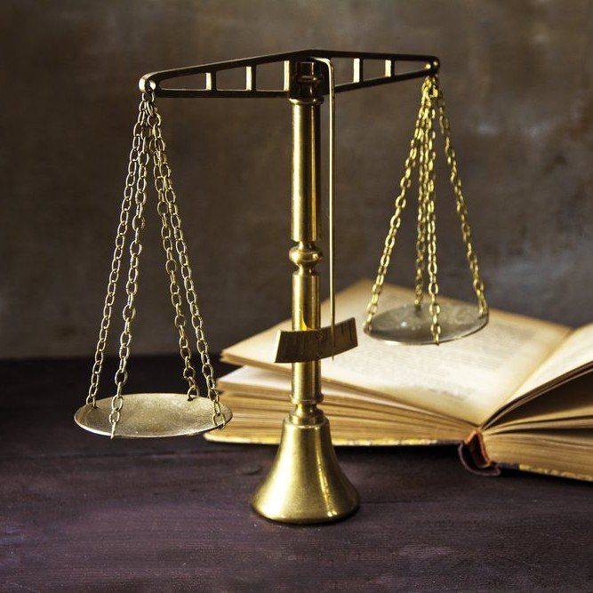 Golden scales of justice in front of an open law book on a dark table