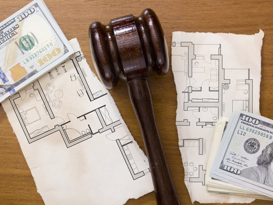 Judge hammer laying between two stacks of money and a ripped house plan