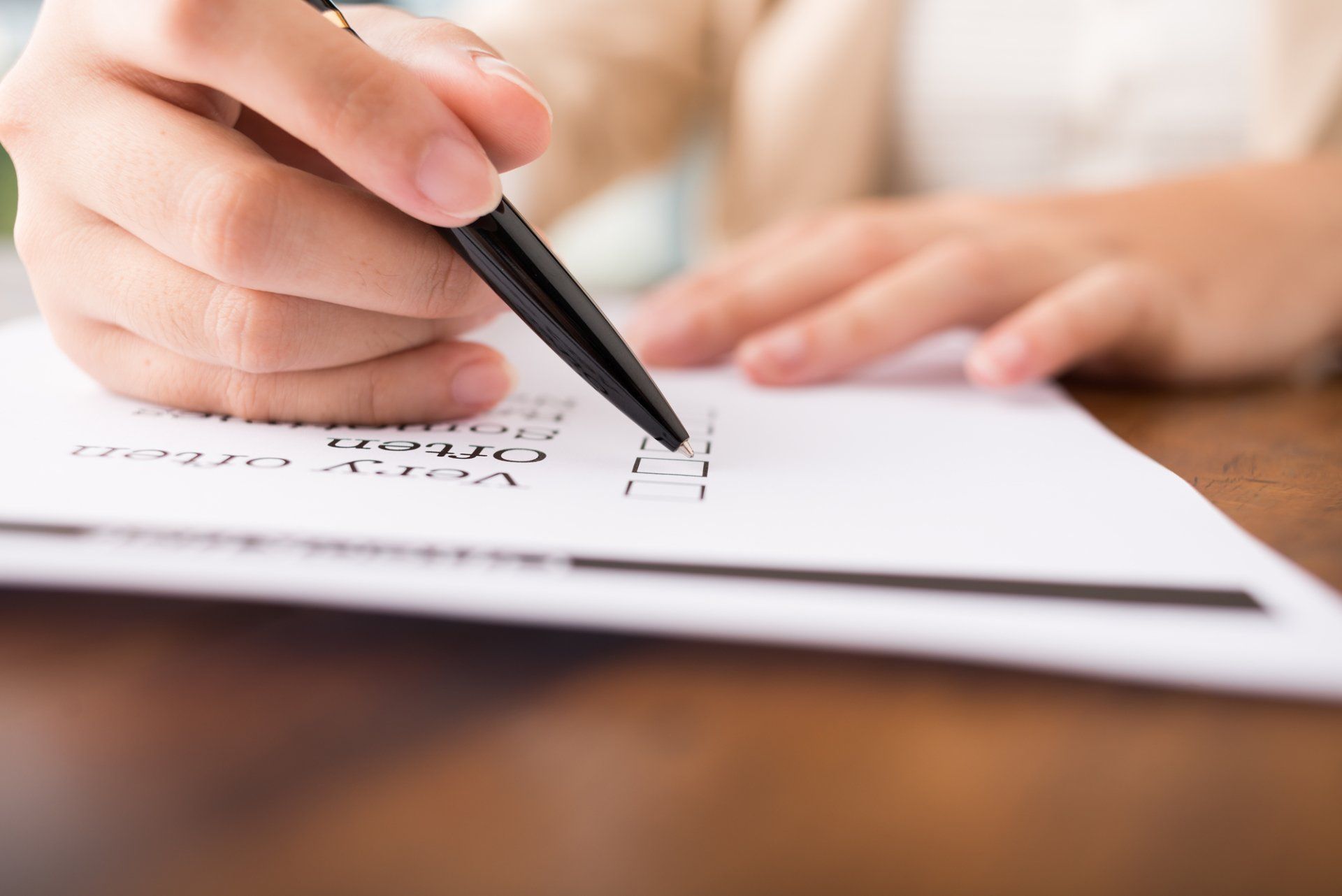Hand writing on a paper form with a black pen at a desk
