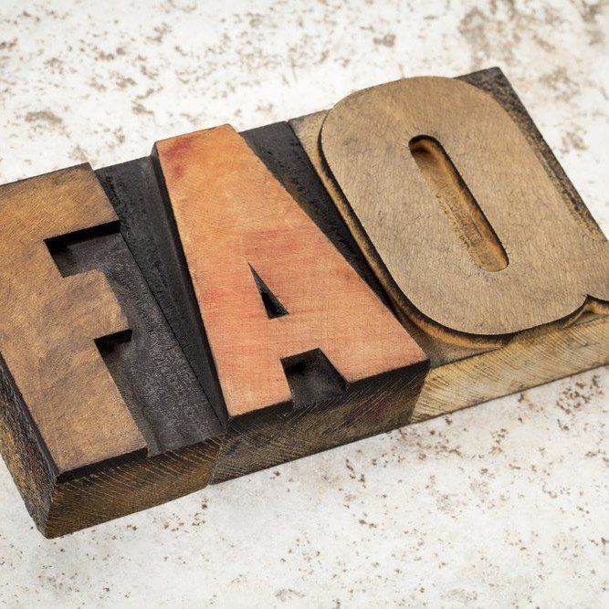 Wooden block letters spelling “FAQ” in black, orange, and tan on a speckled surface