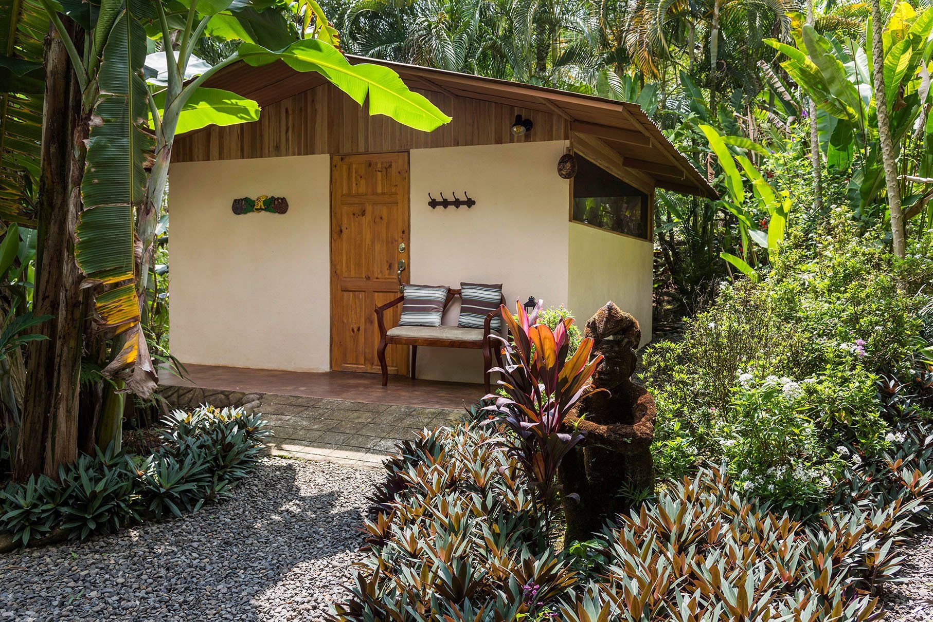 a small house in the middle of a lush green forest with a bench in front of it .