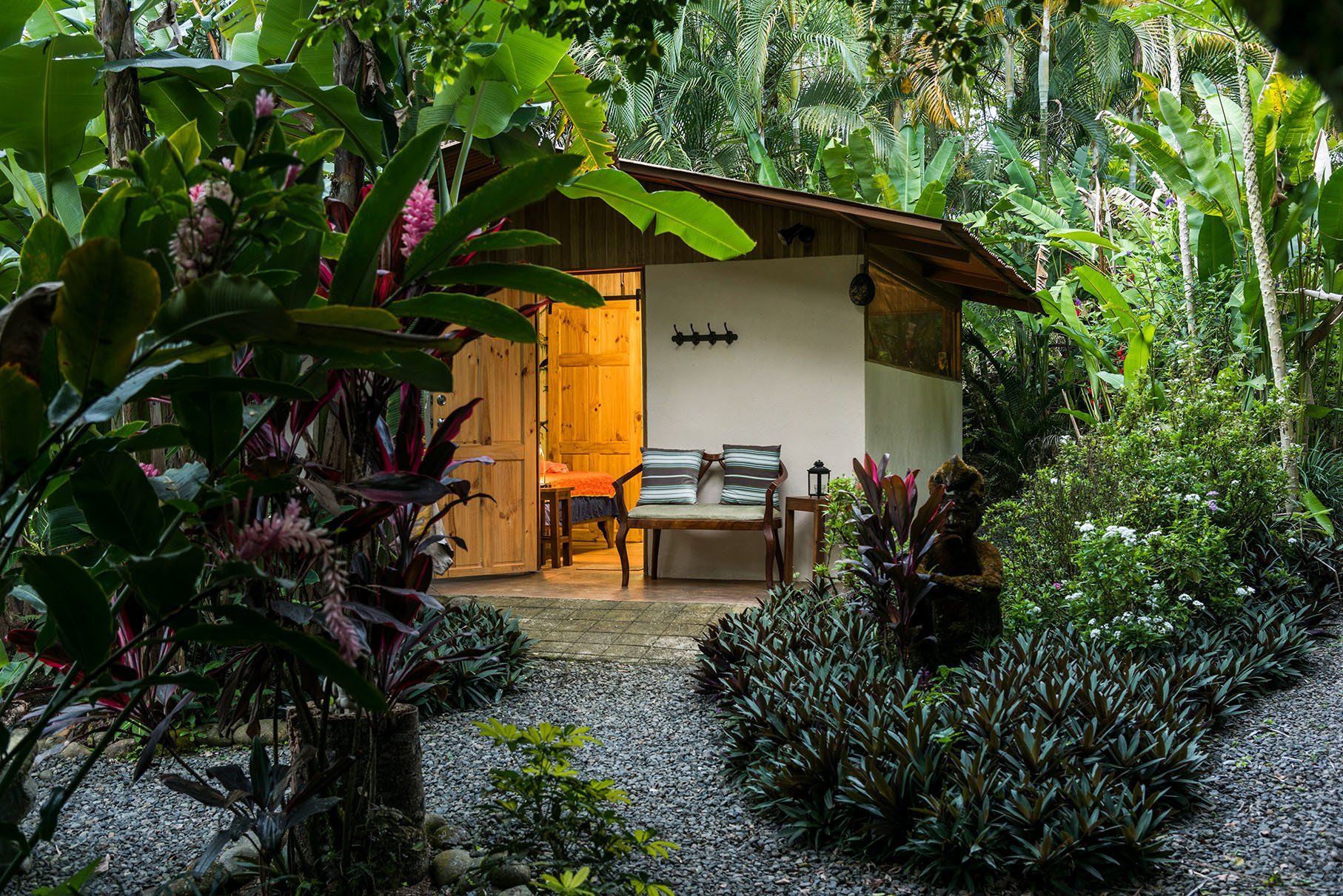 a small house in the middle of a lush green forest with a bench in front of it .