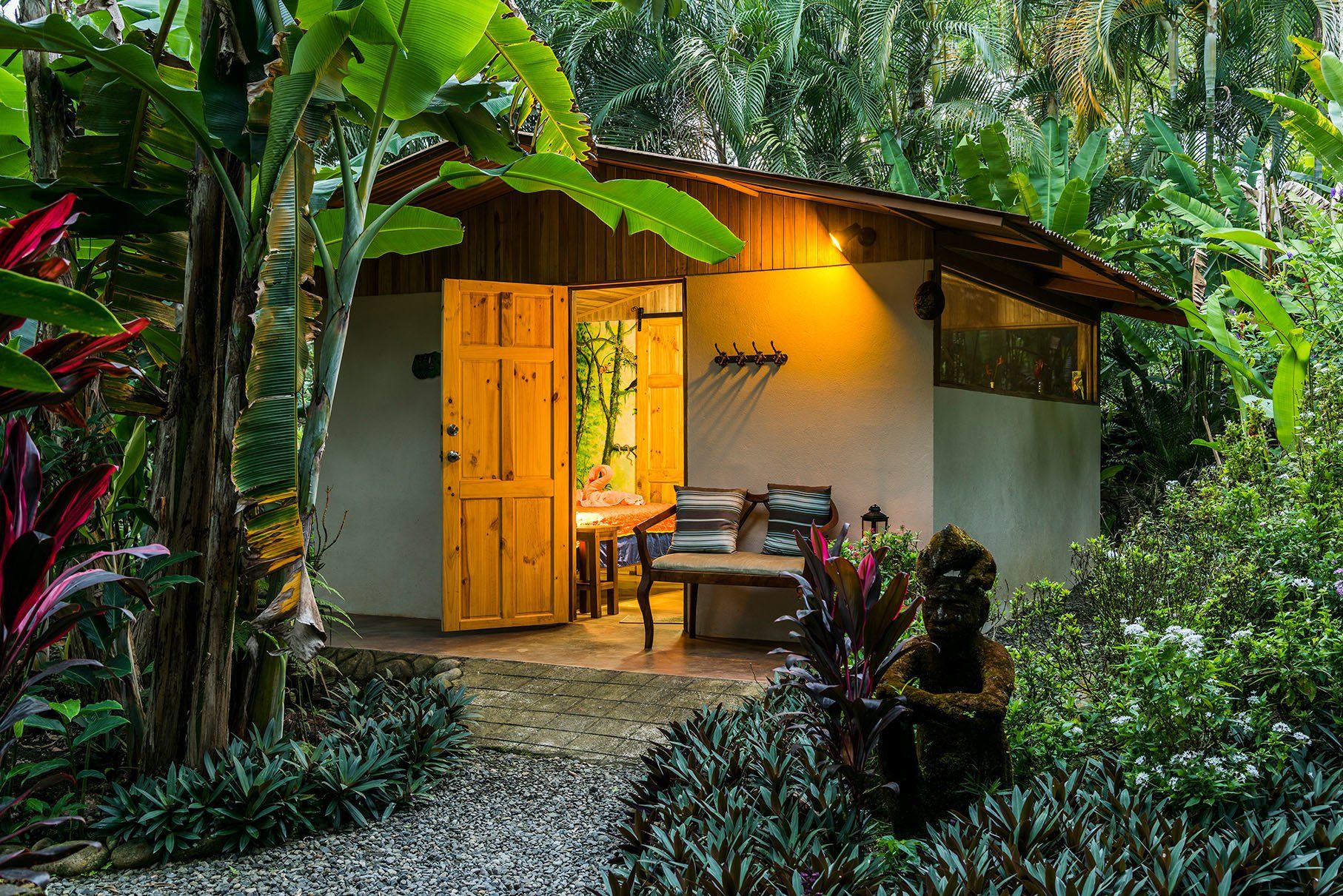a small house in the middle of a lush green forest with a bench in front of it .