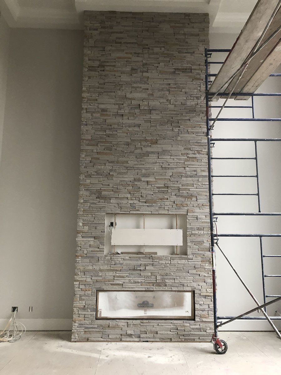Stone veneer fireplace under construction, with scaffolding. Gray and white tones.