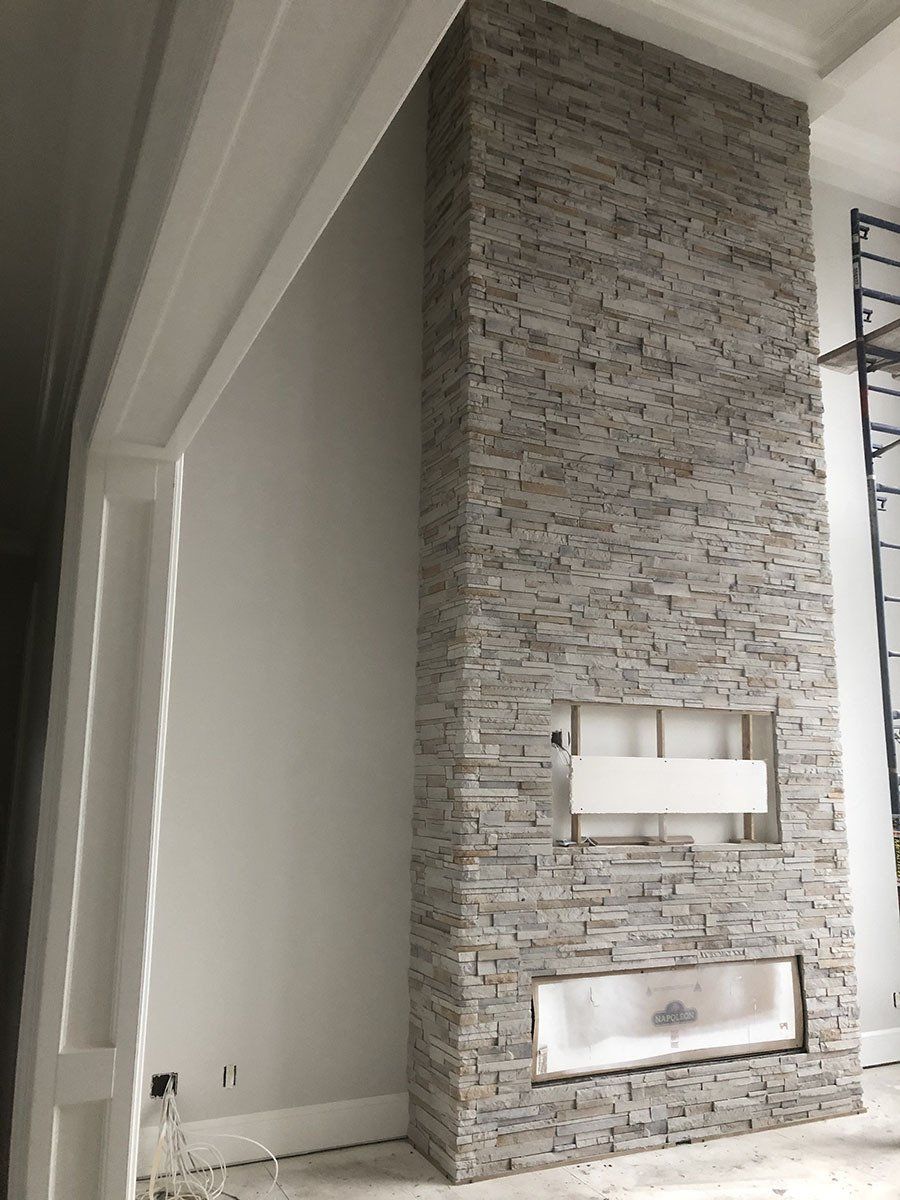 Cheminée en pierre en construction, avec une ouverture rectangulaire blanche prévue pour un futur foyer. Pierre gris clair avec encadrement blanc.