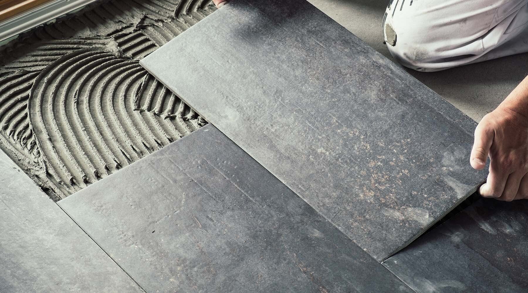 Person installing dark grey tile with mortar on floor.